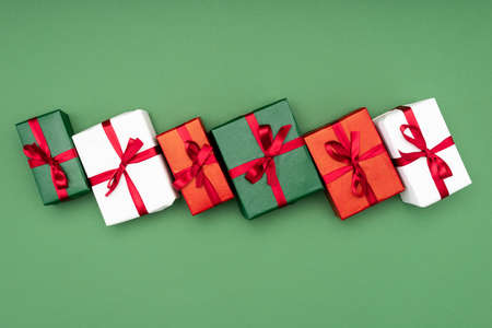 top view of multicolored gift boxes with red ribbons on green background