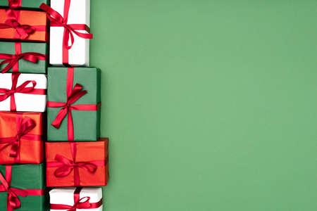 top view of multicolored gift boxes with red ribbons on green background with copy space