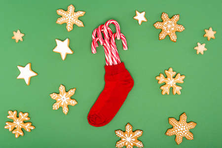 top view of red christmas stocking with candy canes near backed stars and snowflakes on green...