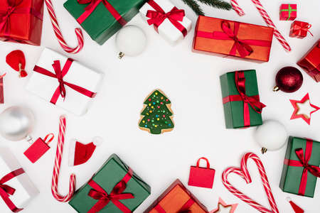 top view of gingerbread christmas tree surrounded by gift boxes and baubles on white background