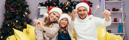 happy family in santa hats holding sparklers in decorated living room, bannerの写真素材