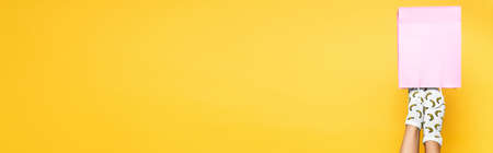 Woman wearing socks, putting legs in pink paper bag isolated on yellow background, banner