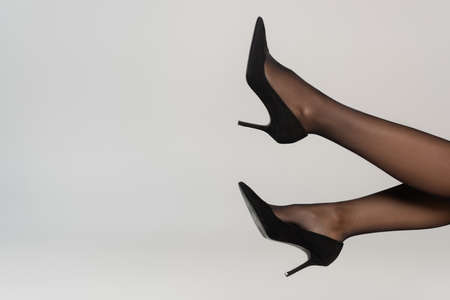 Partial view of woman with legs in air, wearing black tights and shoes with heels isolated on gray