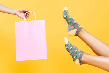 Cropped view of female legs in socks with pineapples print near pink paper bag isolated on yellowの写真素材