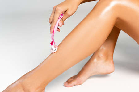 Cropped view of woman shaving smooth leg with safety razor on grayの写真素材