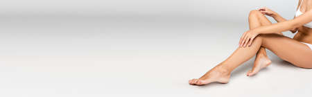 Woman holding hands on knee, while sitting with smooth legs on gray, bannerの写真素材