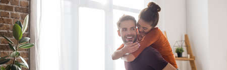 joyful woman piggybacking on happy boyfriend at home, banner