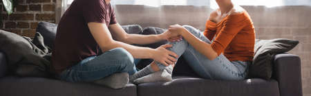 cropped view of young couple holding hands while sitting on sofa at home, banner