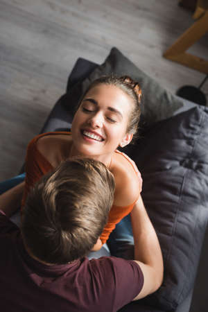 overhead view of cheerful woman with closed eyes embraced by boyfriend at home