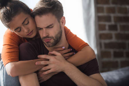responsive woman embracing frustrated man sitting with closed eyes