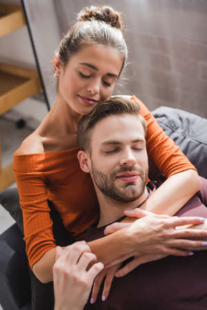 happy woman embracing boyfriend while resting on sofa with closed eyes