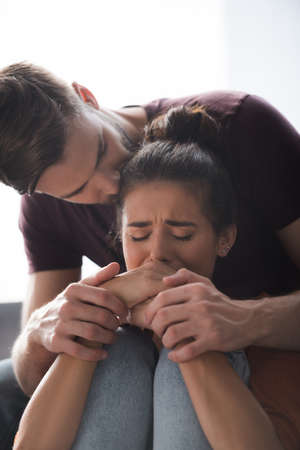 tender man touching hands of depressed girlfriend crying with closed eyes