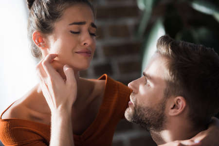 tender man touching face of crying girlfriend while calming her at home