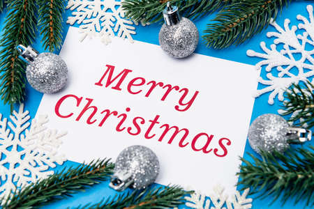 top view of snowflakes, silver baubles and spruce with merry Christmas card on blue backgroundの写真素材