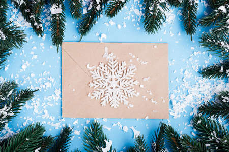 Top view of envelope, decorative snowflake and pine branches with artificial snow on blue backgroundの写真素材