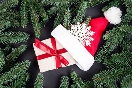 Top view of pine branches, gift box, santa hat and decorative snowflake on black background, new year conceptの写真素材