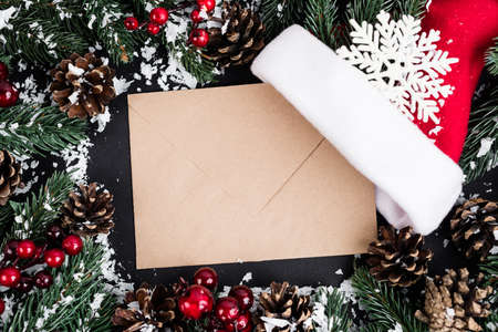 Top view of envelope, santa hat and decorative snowflake near fir branches and pine cones on black backgroundの写真素材