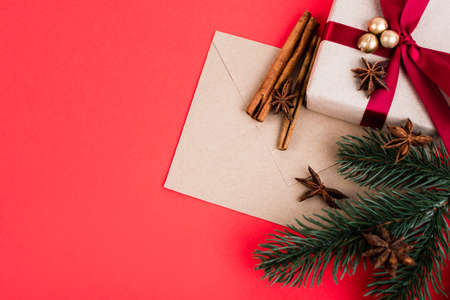 Top view of gift with envelope, cinnamon sticks, anise stars and pine branch on red backgroundの写真素材