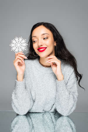 pleased woman with red lips holding decorative snowflake isolated on grayの写真素材
