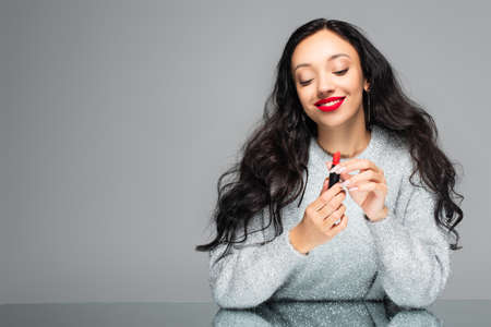 happy woman with red lips holding lipstick isolated on grayの写真素材