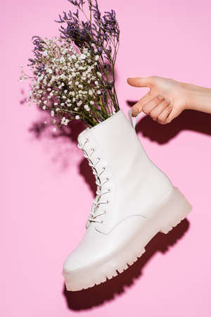 cropped view of woman holding white boot with wildflowers on pink backgroundの写真素材