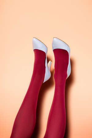 cropped view of female legs in red tights and blue shoes on peach backgroundの写真素材