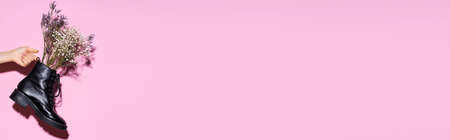 cropped view of woman holding black boot with wildflowers on pink background, bannerの写真素材