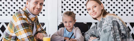 Smiling girl holding pen and sitting near man in checkered shirt and woman in military uniform at table, bannerの写真素材