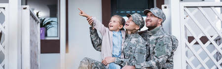 Happy military mother and father sitting near daughter pointing with finger, on backyard, bannerの写真素材