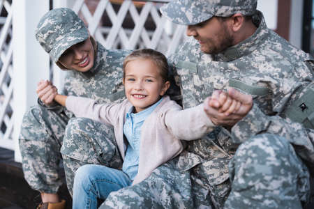 Happy daughter with outstretched hands, sitting with mother and father in military uniforms