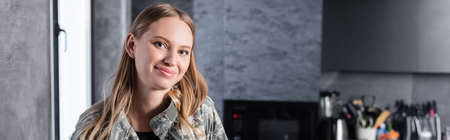 Adult woman with blonde hair looking at camera with blurred kitchen on background, bannerの写真素材