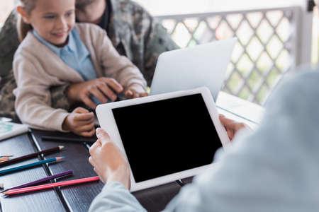 Woman holding digital tablet with blank screen with blurred military man and daughter on backgroundの写真素材