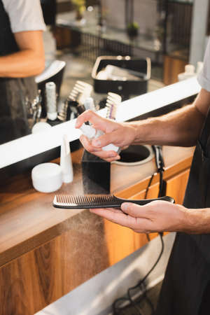 cropped view of hairstylist disinfecting scissors with antiseptic spray at workplace