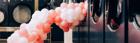 pink balloons near modern washing machines in laundromat, banner