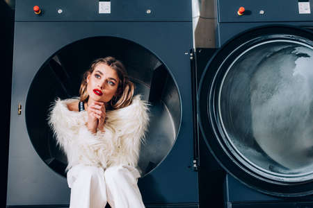 dreamy woman in white faux fur jacket sitting in public washing machine