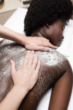 Close up view of masseur massaging african american woman with scrub in spa salon