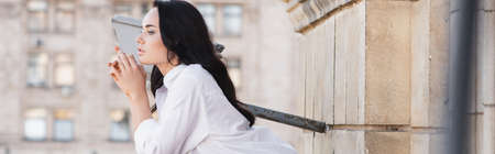 side view of brunette woman standing on balcony and looking away, horizontal banner