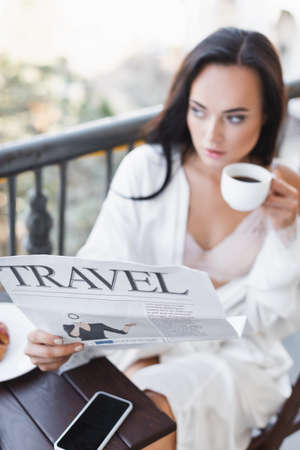 brunette woman in white robe sitting on balcony and reading newspaperの写真素材