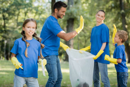 girl looking at camera while parents holding recycled bag and giving high five on blurred background, ecology conceptの写真素材