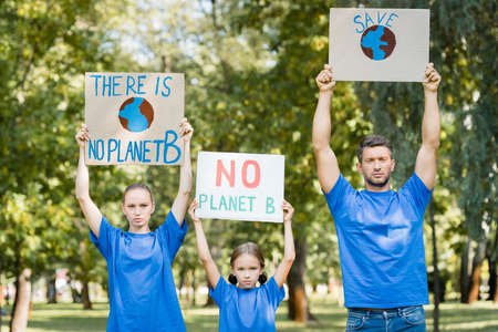 family of volunteers holding placards with globe, save, and no planet b inscription in raised hands,...