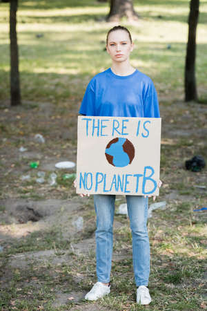 woman looking at camera while holding placard with globe and there is no planet b inscriptionの写真素材