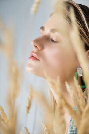 young woman with closed eyes near wheat spikelets on blurred foregroundの写真素材
