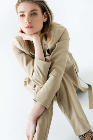 stylish and dreamy model in beige suit sitting on whiteの写真素材