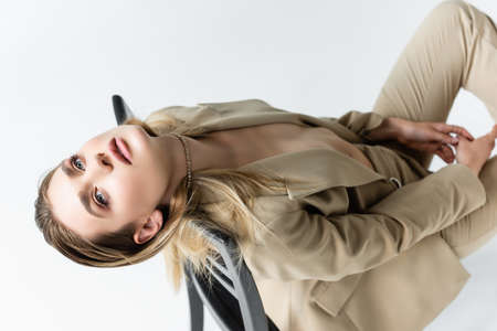young model in beige suit posing on wooden chair isolated on white