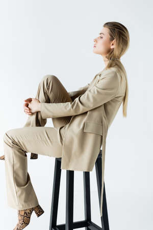 profile of young model in suit poising while sitting on stool on white backgroundの写真素材