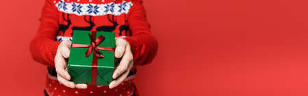 Cropped view of gift box in hands of senior man on blurred background isolated on red, banner