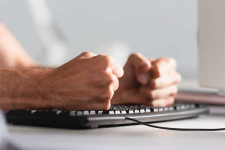 Cropped view of businessman beating computer keyboard in office
