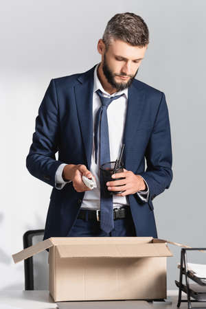 Fired businessman holding stationery near cardboard box in officeの写真素材