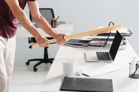 Cropped view of businessman beating laptop with baseball bat near paper folder on blurred foregroundの写真素材