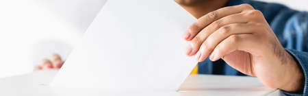 cropped view of man inserting ballot into polling box, banner